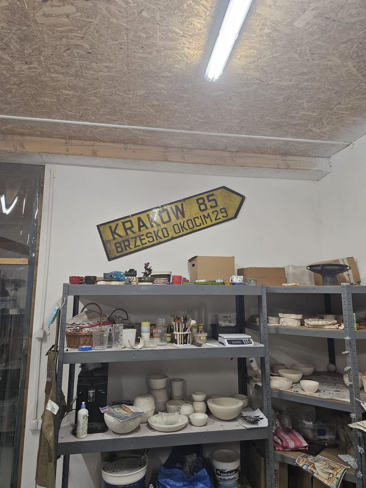 Regał z ceramiką i drogowa tablica Kraków 85 w pracowni